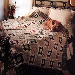 May include: A brown and white quilt with a geometric pattern of squares and arrows. The quilt is on a bed with a brown dog lying on it.