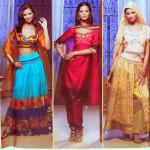 Op de afbeelding: Drie etnische outfits. De eerste heeft een crop top en een lange rok in oranje, blauw en rood. De tweede is een rode jurk met gouden borduursel. De derde is een gouden rok en top met een hoofdbedekking.