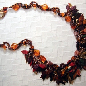May include: A multi-strand necklace with brown, gold, and red beads and charms. The necklace features a cluster of leaf-shaped charms at the bottom.
