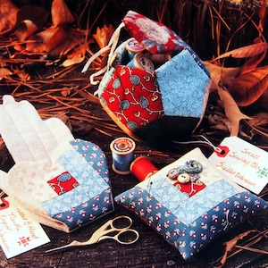 Peut inclure: Ensemble d'articles de couture faits à la main, dont un coussin à épingles, un protège-aiguilles et une petite boîte à couture. Les articles sont en tissu à motifs. Des ciseaux dorés et des bobines de fil sont également présents.