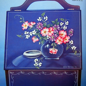 May include: A blue wooden box with a handle, painted with a floral still life. The box has a white painted border and a decorative floral design on the bottom. The text "YARN BOX WITH STILL LIFE pages 44, 45, 46" is printed on the top right corner of the box.