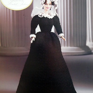 Puede incluir: Muñeca de la colección First Ladies of America, vestida con un largo vestido negro con ribetes de encaje blanco. La muñeca tiene un gorro a juego y un cuello de encaje blanco. La imagen incluye el texto "First Ladies of America Collection" y el nombre "Rachel Jackson".