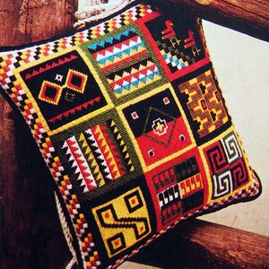 Puede incluir: Una almohada colorida con un patrón geométrico en tonos de rojo, amarillo, verde, negro y blanco. La almohada está hecha de tela y tiene un borde de flecos.
