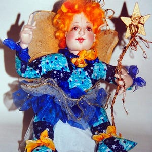 May include: A handmade doll with orange hair, a blue and white patterned dress, and gold wings. The doll is holding a gold star-shaped wand.