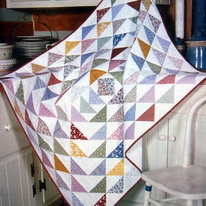 May include: A handmade quilt featuring a patchwork design of colorful triangles on a white background. The quilt has a red border and showcases various patterns and colors, including blue, pink, yellow, and floral prints. This cozy quilt is perfect for adding a touch of warmth and style to any home.