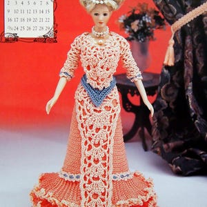 May include: A doll wearing a peach-colored crocheted dress with a blue accent. The dress has a long, openwork panel down the front and a ruffled skirt. The doll has blonde hair and a pearl necklace. A calendar for June 1996 is in the background.