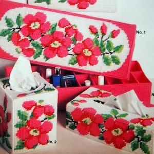 Peut inclure: Ensemble de boîtes à mouchoirs et de rangement en point de croix. Les motifs présentent des fleurs rouges vives avec des feuilles vertes sur fond blanc. Les boîtes sont de formes et tailles variées, avec un bord rose assorti.