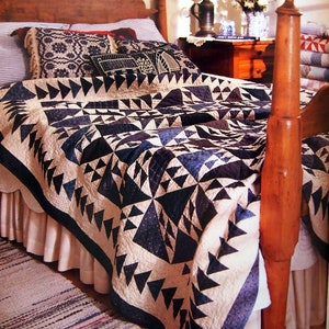 May include: A white and blue quilt with a geometric pattern of triangles. The quilt is on a bed with a wooden headboard and a white bed skirt.