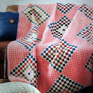 May include: A pink quilt with a checkered pattern in red, blue, and white. The quilt is folded and draped over a brown leather couch.