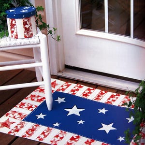 Può includere: Un tappetino per la porta a tema patriottico con un centro blu con stelle bianche, circondato da un bordo a strisce rosse e bianche. Una scatola rotonda abbinata con un coperchio blu stellato e lati a motivi rossi e bianchi.