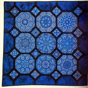 May include: A square quilt featuring a repeating pattern of large octagonal blocks and smaller diamond-shaped accents. The fabric displays intricate blue and white mandala-style motifs, connected by solid dark blue sashing and borders.
