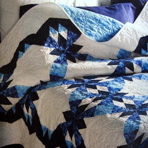 Peut inclure: Une couette blanche avec un motif d'étoiles bleues et noires. La couette est pliée et drapée sur un lit avec des oreillers.