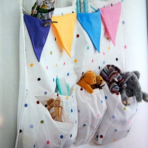 May include: White fabric wall organizer with colorful polka dots and three pockets. The organizer has a wooden rod at the top and features colorful triangle flags. The pockets contain stuffed animals, toys, and other items.