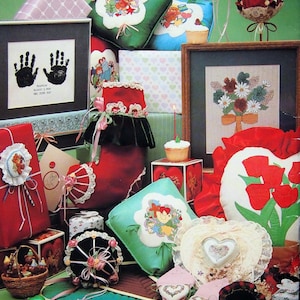 May include: A selection of handcrafted items, including framed handprints, embroidered cushions, and gift boxes. The colour scheme features red, green, and white, with floral and heart designs. A cupcake with a lit candle is also visible.