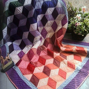 May include: A purple, blue, and pink quilt with a geometric pattern of diamonds. The quilt is folded in half and has a purple border.