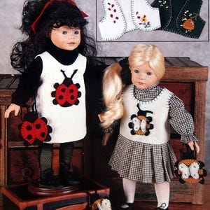 May include: Two dolls wearing felt dresses with ladybug and butterfly appliques. The dolls are holding matching felt purses with ladybug and butterfly designs. The dolls are standing on a wooden surface with a suitcase in front of them.