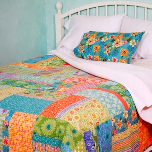 May include: A white bed with a patchwork quilt in shades of blue, green, orange, and pink. The bed has a white headboard and a white pillow with a floral print.