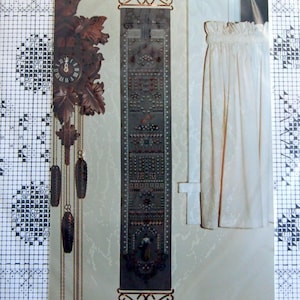 May include: A dark brown wooden cuckoo clock with decorative leaves and hanging weights. A long, narrow, embroidered tapestry with ornate patterns and a figure at the bottom. A cream-colored curtain is visible on the right.