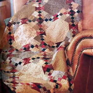 May include: A brown leather armchair with a patchwork quilt draped over it. The quilt is made of various fabrics in shades of brown, red, and cream, with a swirling pattern.