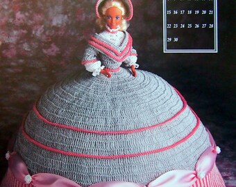 May include: A crocheted doll dress with a gray bodice and a pink and white striped skirt. The doll is wearing a white crocheted hat and has blonde hair. The dress has a pink satin ribbon around the waist. The image includes a calendar for September.