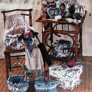 May include: A collection of fabric covered boxes and baskets in various floral patterns and colors. The boxes are shaped like hearts and are decorated with lace and ribbons. The baskets are woven and have fabric lining. The items are arranged on a wooden table and a chair.