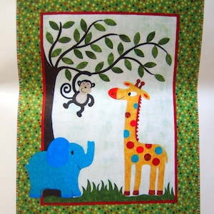 May include: A colorful fabric wall hanging featuring a whimsical jungle scene. It depicts a blue elephant, a giraffe with red, yellow, and blue spots, and a monkey hanging from a tree. The border is green with a polka dot pattern.