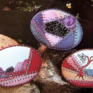 May include: Three oval embroidered artworks. One has a web design, another a mountain scene, and the third a tree. Each has a stitched border and colourful fabric backgrounds, with a variety of colours.