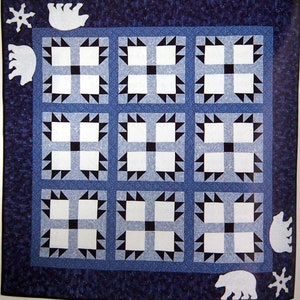 May include: A blue and white quilt with a polar bear design. The quilt is made up of squares with a black and white checkered pattern. The quilt is surrounded by a dark blue border with white snowflakes and polar bears.