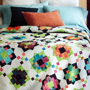 Op de afbeelding: Een wit dekbed met een patchwork-ontwerp met vierkanten in verschillende kleuren, waaronder groen, blauw, roze, oranje en zwart. Het dekbed is opgevouwen op een bed met kussens.