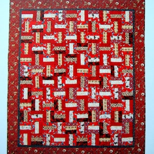 Può includere: Una trapunta di patchwork rosso, bianco e marrone con un motivo geometrico. La trapunta è realizzata con diversi tessuti con motivi e trame differenti.