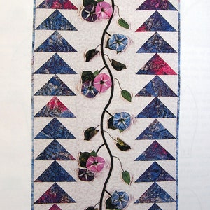 May include: A quilt pattern featuring a vine with blue and pink flowers and leaves, with a row of blue and pink triangles on each side.