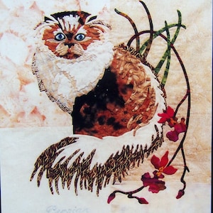 May include: A fabric art piece featuring a Persian cat with blue eyes, brown and white fur, and a fluffy tail. The cat is set against a soft, patterned background with red flowers and the word "Persian" at the bottom.