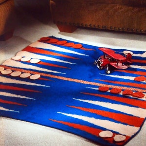 May include: A blue and red rug with white stripes and pink circles. A red toy airplane is on the rug.