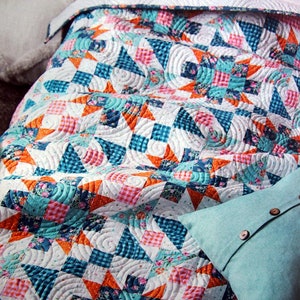 May include: A white quilt with a patchwork design featuring orange, pink, blue, and white fabric. The quilt is quilted with a swirling pattern.