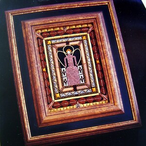May include: A framed needlepoint artwork featuring a stylized angel with wings, wearing a pink dress and a halo. The angel is surrounded by a decorative border with geometric patterns in shades of brown, gold, and white.