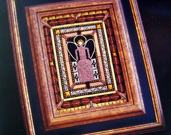 May include: A framed needlepoint artwork featuring a stylized angel with wings, wearing a pink dress and a halo. The angel is surrounded by a decorative border with geometric patterns in shades of brown, gold, and white.