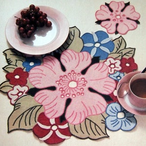 May include: A floral table runner with pink, blue, and red flowers on a beige background. The runner is made of fabric and has a delicate, embroidered design.