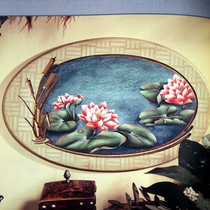 May include: A painted oval wall art piece with a blue background and a border of tan squares. The center of the oval features a water lily scene with pink flowers, green leaves, and brown reeds. The title "Water Lilies" is written in white cursive at the top of the image.