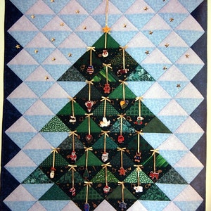 May include: A quilted Christmas tree wall hanging with a blue and white background and a green tree with ornaments. The tree is made of fabric triangles and has a star on top.