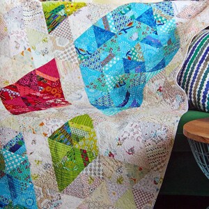 Peut inclure: Une courtepointe colorée en patchwork avec un fond blanc et des formes géométriques dans des tons de bleu, vert et rouge. La courtepointe est drapée sur un canapé et porte le texte "Designer Tonya Alexander (eyecandyquilts.blogspot.com) Machine Quilter Tracey Fisher".