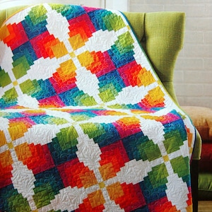 May include: A colorful quilt with a geometric pattern of squares and rectangles in shades of red, orange, yellow, green, blue, and white. The quilt is folded and draped over a green armchair.
