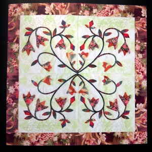 May include: A quilt block with a floral design featuring red, green and white flowers on a light green background. The flowers are arranged in a symmetrical pattern with a central point.