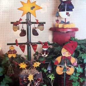 Puede incluir: Una exhibici&oacute;n navide&ntilde;a festiva con un &aacute;rbol de madera adornado con mini-mitones, medias y corazones. Un mu&ntilde;eco de nieve y un hombre de jengibre tambi&eacute;n est&aacute;n presentes. La exhibici&oacute;n incluye un adorno de &aacute;rbol en forma de estrella y otros adornos de estrella y &aacute;rbol.