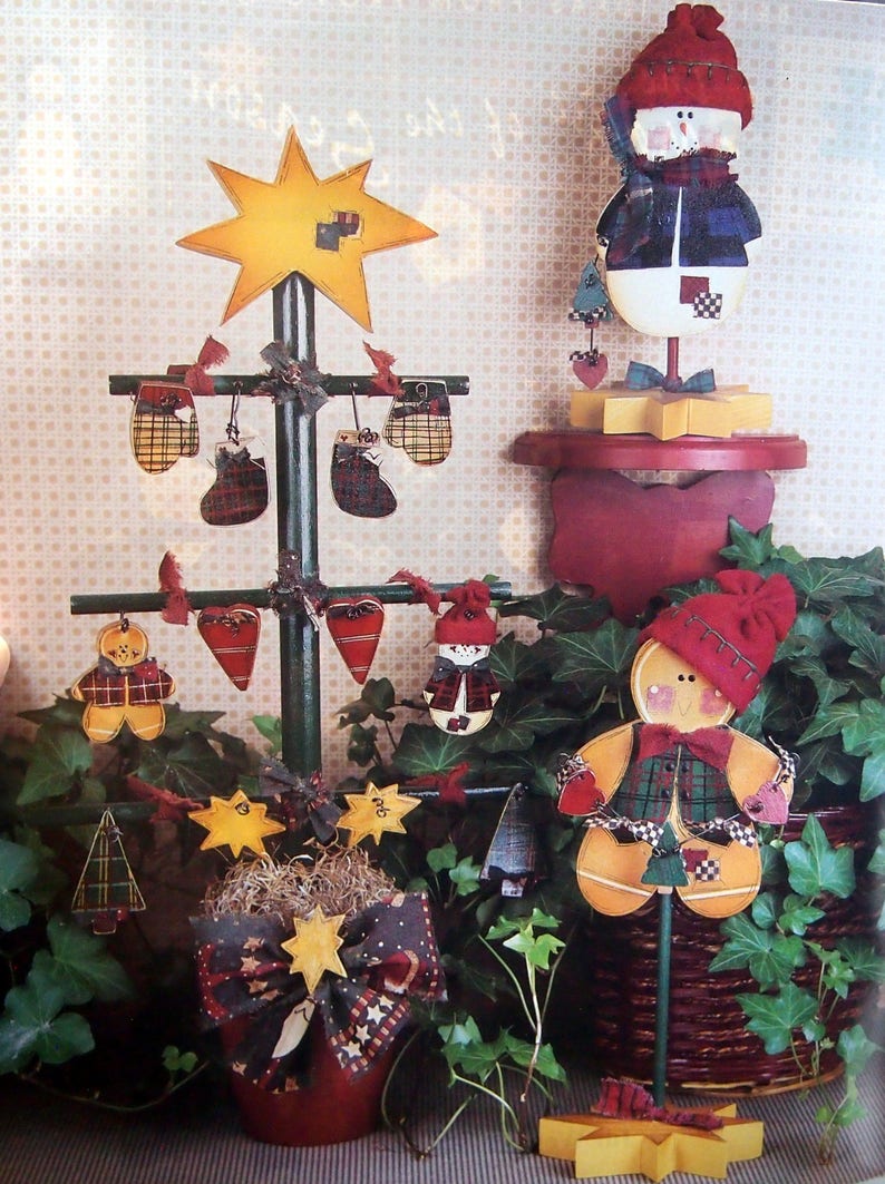 Puede incluir: Una exhibici&oacute;n navide&ntilde;a festiva con un &aacute;rbol de madera adornado con mini-mitones, medias y corazones. Un mu&ntilde;eco de nieve y un hombre de jengibre tambi&eacute;n est&aacute;n presentes. La exhibici&oacute;n incluye un adorno de &aacute;rbol en forma de estrella y otros adornos de estrella y &aacute;rbol.