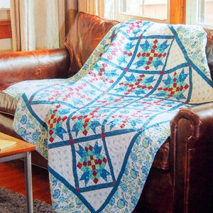 May include: A white, blue and red patchwork quilt with a floral border is draped over a brown leather sofa. The quilt features a star pattern in the centre.