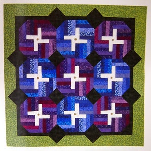 May include: A quilt with a geometric design featuring nine octagons with a white plus sign in the center. The octagons are made of purple, blue, and red fabric strips. The quilt is framed with a black and green border.
