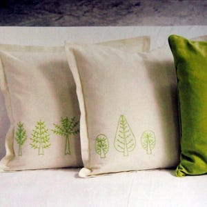 May include: Three white throw pillows with green embroidered trees on them. The pillow on the right has a solid green back.