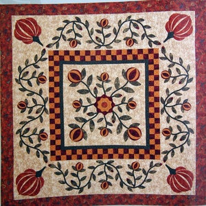 Puede incluir: Una colcha beige con un diseño cuadrado central que presenta un patrón floral estilizado en tonos marrones, naranjas y rojos. El cuadrado está rodeado por un borde de cuadrados naranjas y marrones alternados, y toda la colcha está enmarcada por un borde rojo.