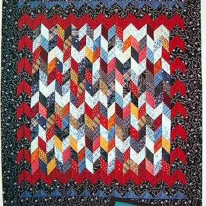 Peut inclure: Une courtepointe colorée avec un motif en chevron dans des tons de rouge, bleu, jaune et blanc. La courtepointe est bordée d'un tissu à motifs noir et bleu.