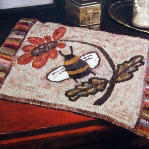 May include: A beige rug with a brown bee and flower design. The rug has a multi-colored striped border.